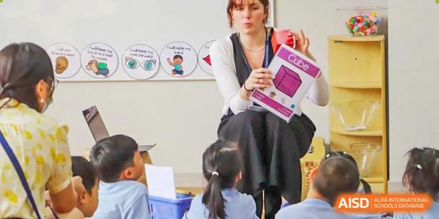 A teacher from Hangzhou International School reading or instructing a group of young students in a classroom.