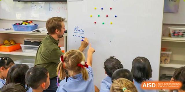 A teacher from Hangzhou International School helping young students write on a whiteboard in a classroom.