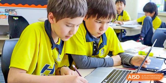 Two students from Hangzhou International School working together on a laptop and writing in a notebook during class.