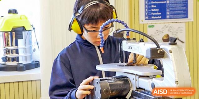 A male student from Hangzhou International School using a 3D printer or similar technology while wearing headphones.