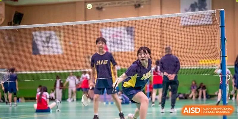 Badminton players from Hangzhou International School competing in a doubles match on an indoor court.