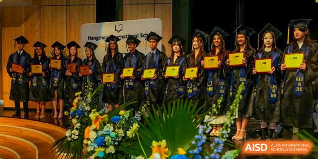 A group of Hangzhou International School graduates in caps and gowns posing with their diplomas during a graduation ceremony.