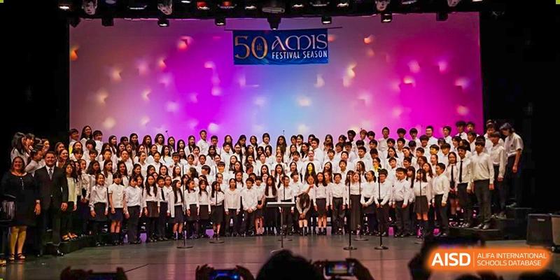 A large choir or music group from Hangzhou International School performing on stage under bright lights.