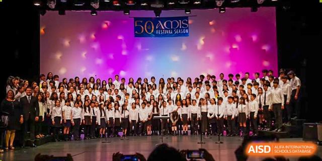 A large choir or music group from Hangzhou International School performing on stage under bright lights.