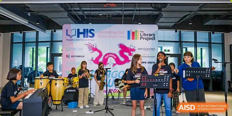 Students from Hangzhou International School performing live music on a stage with guitars and a microphone stand at a school event.