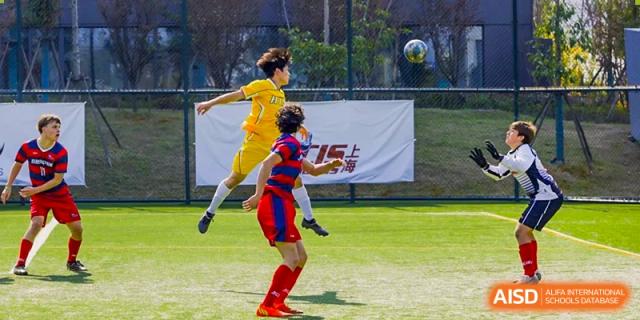 Hangzhou International School students playing soccer, with one student in red kicking the ball and another in yellow jumping.