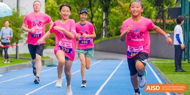 Students from Hangzhou International School running on a blue track during an outdoor sports event.