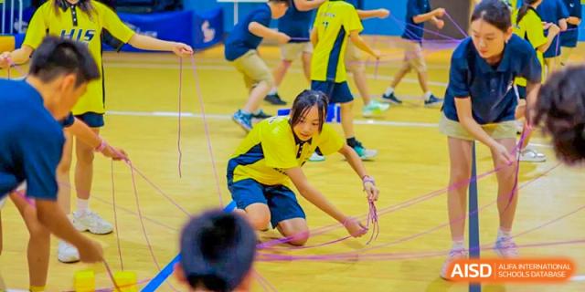 A student from Hangzhou International School, wearing a yellow jersey, reaching for a rope or band during an indoor activity.