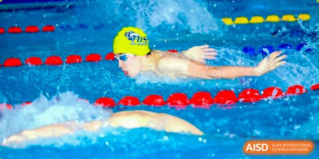 A swimmer from Hangzhou International School wearing a yellow cap and goggles performing the freestyle stroke in a pool.