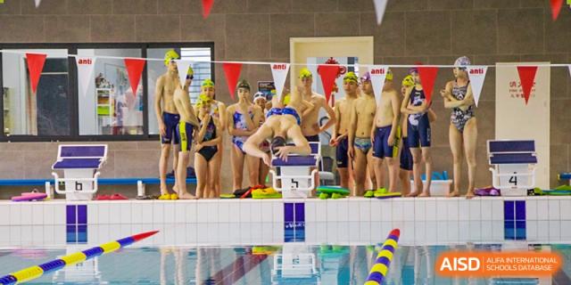 Hangzhou International School swimmers standing on the starting blocks before a race at an indoor pool.