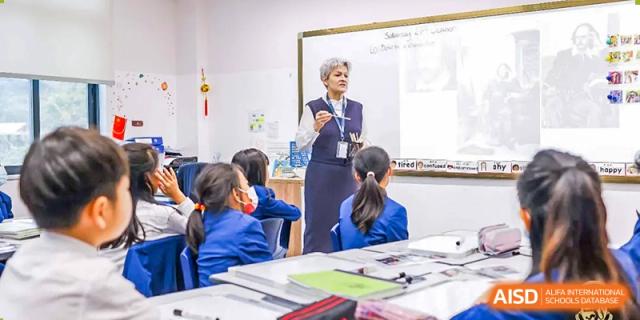 A teacher speaking to a class of young students seated at desks in a bright classroom at Harrow LiDe School Chongqing (AISL Harrow Chongqing).