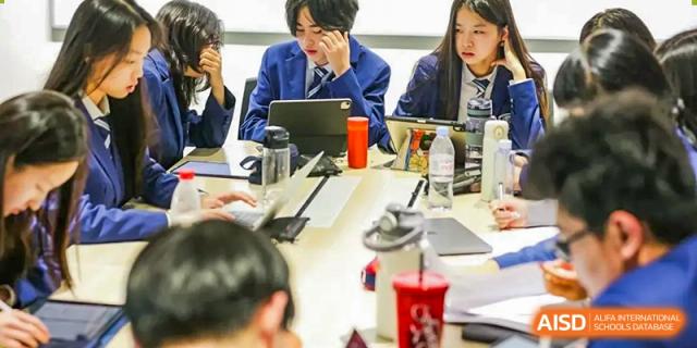 High school students at Harrow LiDe School Chongqing (AISL Harrow Chongqing) collaborating around a table, using a digital tablet for their study.