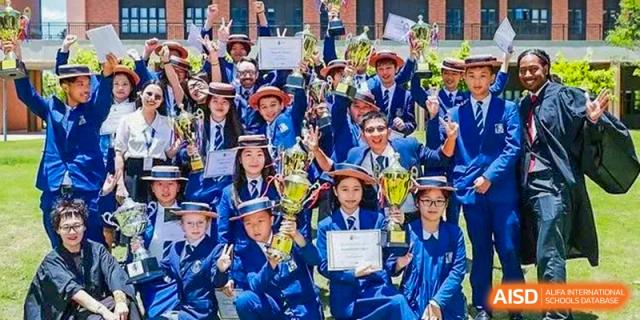 A large group of students from Harrow LiDe School Chongqing (AISL Harrow Chongqing) in academic dress celebrating with trophies and certificates outdoors.