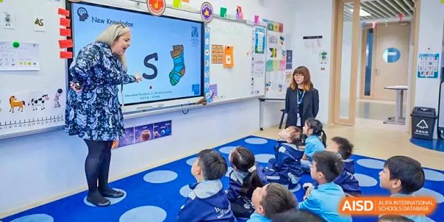 Young students sitting on the floor, interacting with a colorful digital lesson on a large screen at Harrow LiDe School Chongqing (AISL Harrow Chongqing).