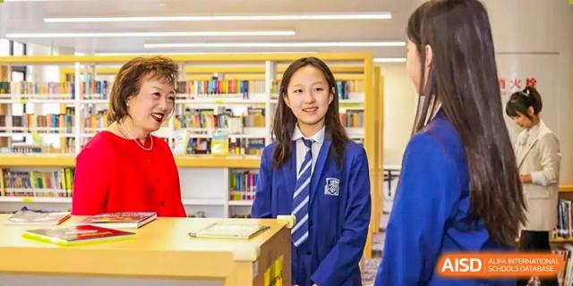 A smiling female student from Harrow LiDe School Chongqing (AISL Harrow Chongqing) in uniform standing in the school library or resource center.
