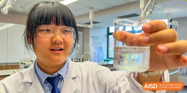 A student from Harrow LiDe School Chongqing (AISL Harrow Chongqing) wearing a lab coat and safety goggles while conducting an experiment in a science laboratory.