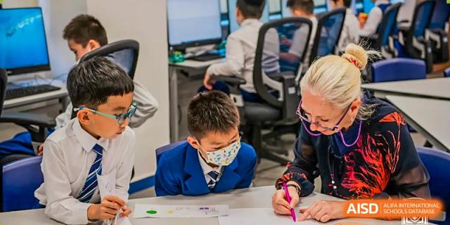 A young student from Harrow LiDe School Chongqing (AISL Harrow Chongqing) wearing a face mask and working on a creative project with a group at a table.