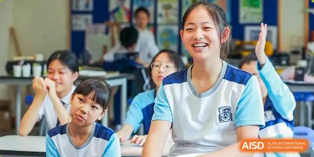A smiling female student from Harrow LiDe School Chongqing (AISL Harrow Chongqing) looking directly at the camera while sitting in a classroom with other students.