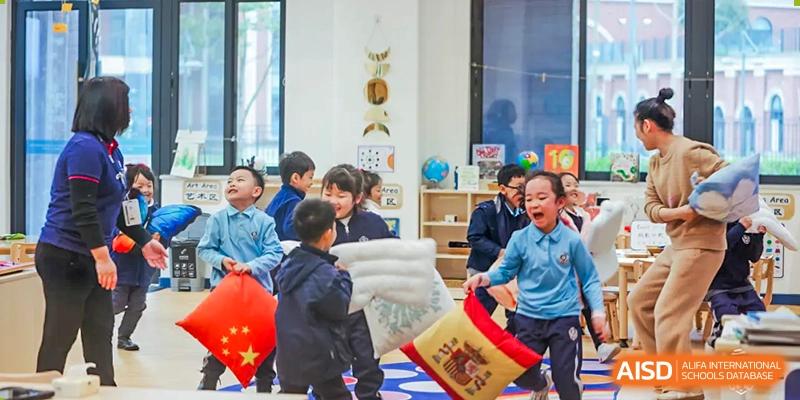 Young students at Harrow LiDe School Chongqing (AISL Harrow Chongqing) enthusiastically participating in a fun, active game with cushions in a bright classroom.
