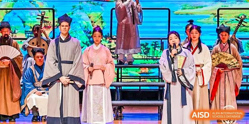 A student from Harrow LiDe School Chongqing (AISL Harrow Chongqing) in traditional clothing standing on stage during a performance or cultural event.