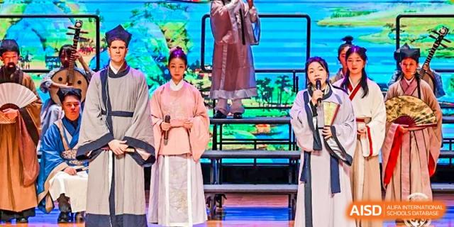 A student from Harrow LiDe School Chongqing (AISL Harrow Chongqing) in traditional clothing standing on stage during a performance or cultural event.