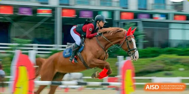 A student representing Harrow LiDe School Chongqing (AISL Harrow Chongqing) jumping a fence on horseback during an equestrian competition.