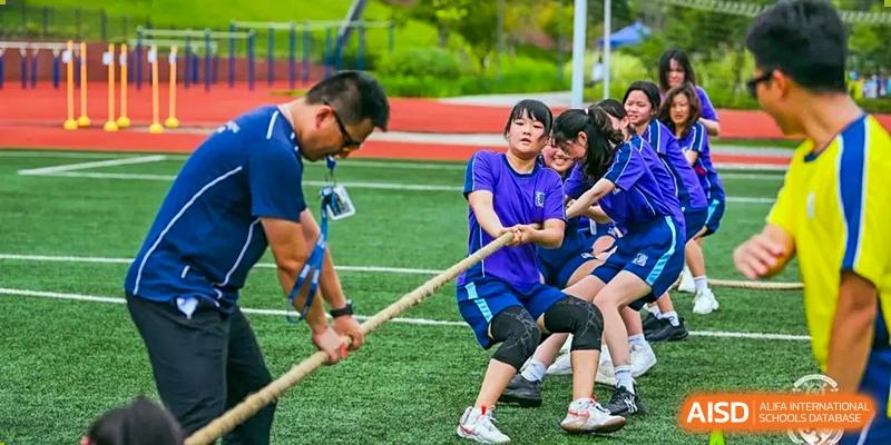 Students and a teacher from Harrow LiDe School Chongqing (AISL Harrow Chongqing) enthusiastically participating in a tug-of-war competition on a sports field.
