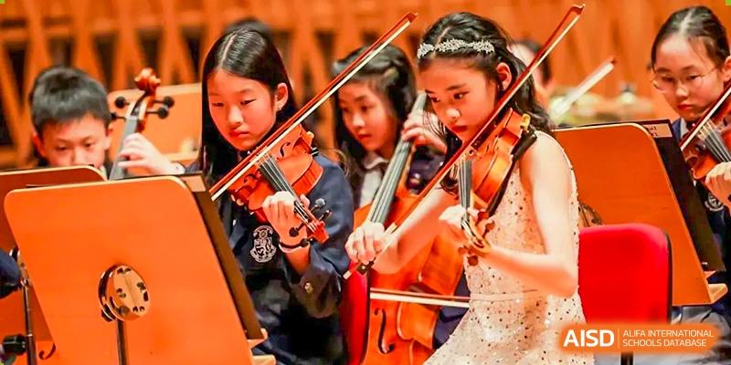 Three young students from Harrow LiDe School Chongqing (AISL Harrow Chongqing) intently playing the violin during a musical practice or concert.