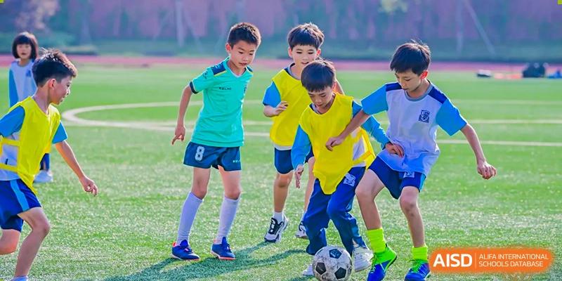 Young students from Harrow LiDe School Chongqing (AISL Harrow Chongqing) playing soccer/football on a green field.