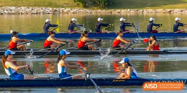 Students from Harrow LiDe School Chongqing (AISL Harrow Chongqing) practicing rowing or sculling in a narrow boat on a lake.