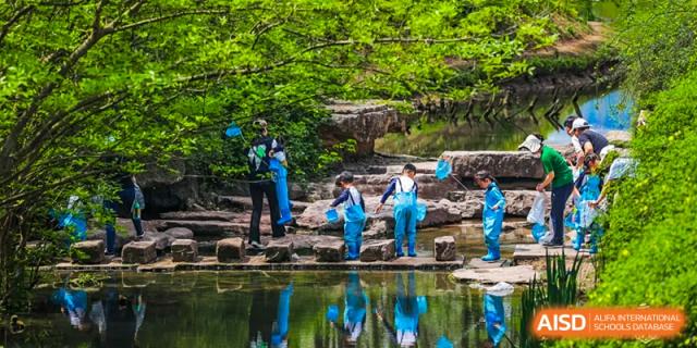 Students from Harrow LiDe School Chongqing (AISL Harrow Chongqing) participating in an outdoor activity, standing by a body of water with trees in the background.