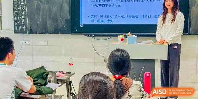 Student viewed from behind, sitting in a classroom looking at a presentation on a large screen displaying Chinese text Hefei No.6 High School International Department.