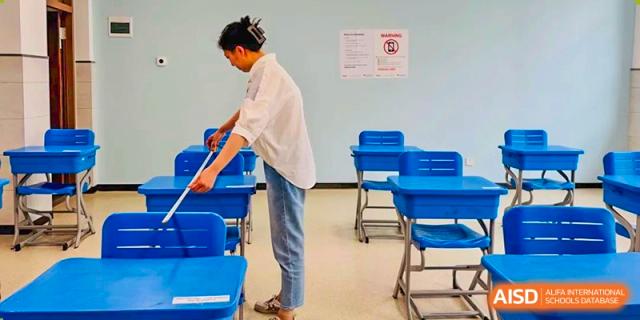 A teacher adjusting a student's blue desk and chair in a quiet classroom, preparing for a lesson at the Hefei No.6 High School  International Department.