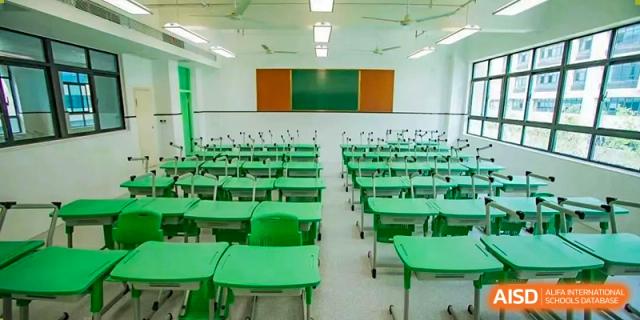 A brightly lit, empty classroom with rows of green desks and chairs Hefei No.6 High School International Department.