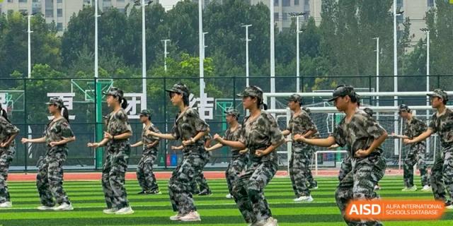 A group of students in camouflage practice uniforms marching or exercising in formation on the outdoor sports field at the  Hefei No.6 High School International Department .
