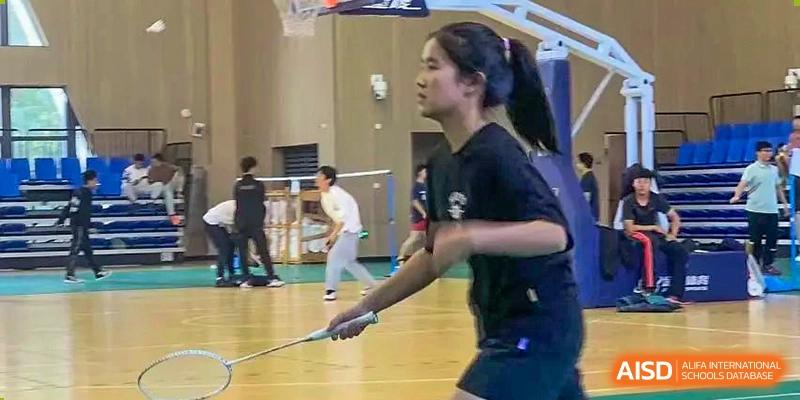 A female student playing badminton in the indoor gymnasium, focused on hitting the shuttlecock at the Hefei No.6 High School International Department.