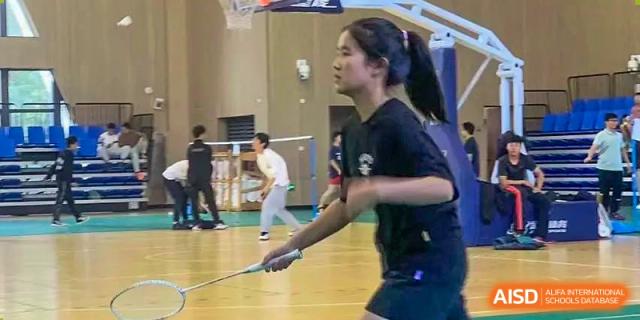 A female student playing badminton in the indoor gymnasium, focused on hitting the shuttlecock at the Hefei No.6 High School International Department.