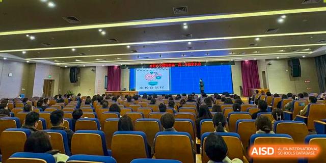 A large audience of students seated in the auditorium, facing a stage with a screen presentation during a school event or lecture at the Hefei No.6 High School International Department.