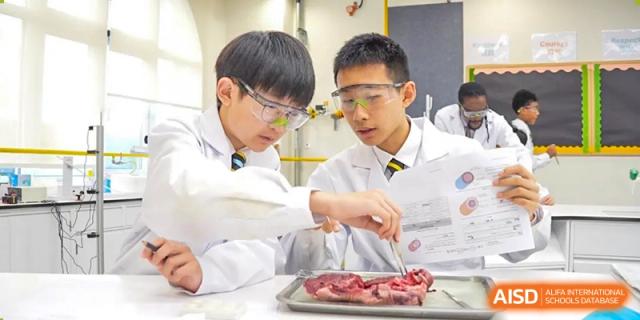 Two male students from Hiba Academy Nantong wearing lab coats and goggles, performing a dissection or scientific experiment in a laboratory.