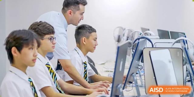 A teacher from Hiba Academy Nantong assisting two male students working on laptops in a technology or computer lab.