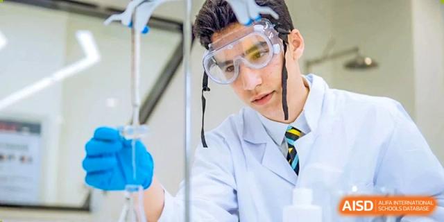 A male student from Hiba Academy Nantong in a lab coat and safety goggles, working with blue liquid in a beaker during a science experiment.