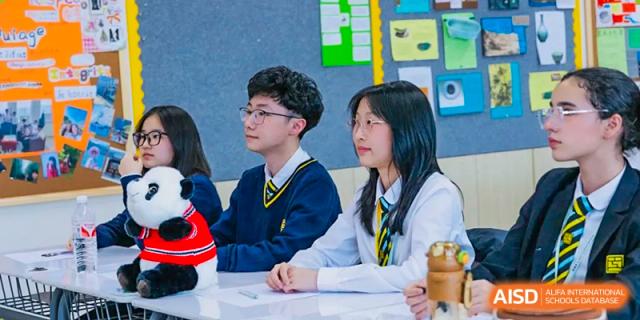 Three students from Hiba Academy Nantong, two male and one female, sitting at a desk and listening attentively in a classroom.