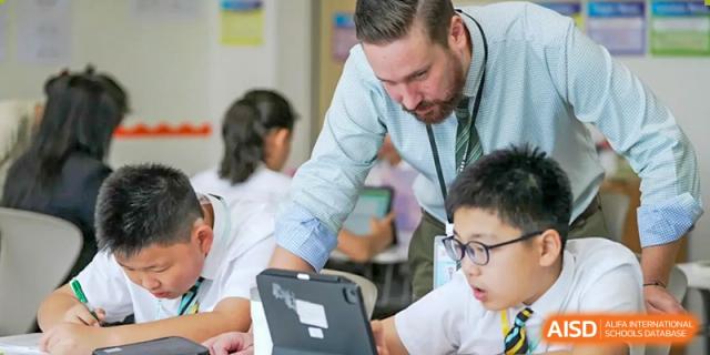A male teacher at Hiba Academy Nantong supervising and helping students who are using tablets in a classroom setting.