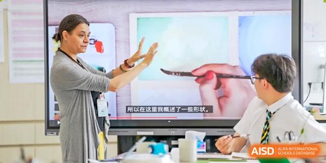 Students at Hiba Academy Nantong watching an educational video on a screen, which shows a close-up of a hand painting a delicate line.