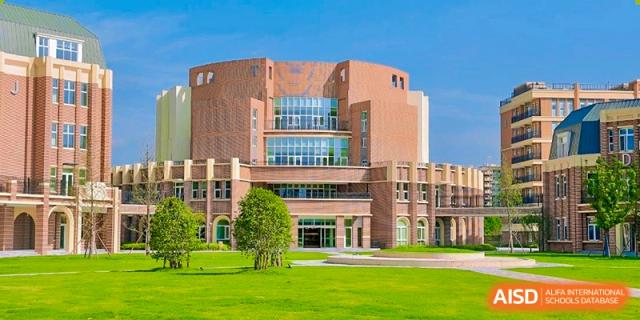 The striking contemporary and red-brick architecture of a main building at Hiba Academy Nantong, featuring large windows and a curving facade with a large green lawn in the foreground.