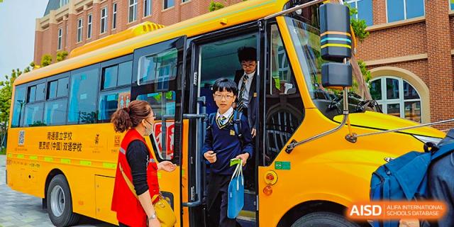 A student from Hiba Academy Nantong in uniform exiting a bright yellow school bus, with a staff member standing near the door.