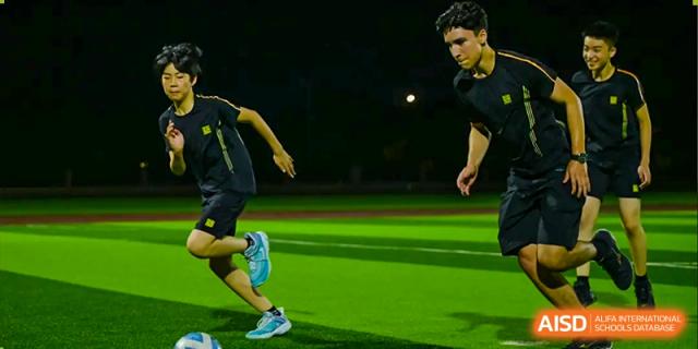 Close-up of a student's legs from Hiba Academy Nantong running on a bright green field at night, possibly during a sports practice or game.