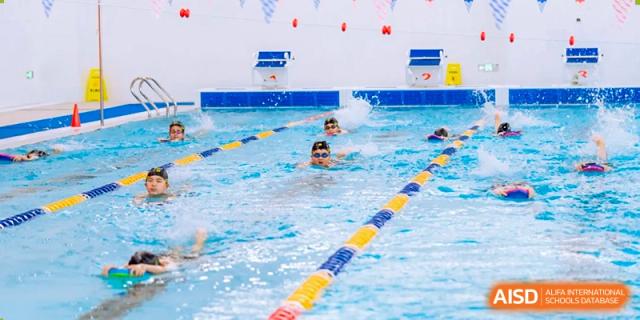 Multiple students from Hiba Academy Nantong swimming laps in a competition pool, with lane ropes visible separating them.
