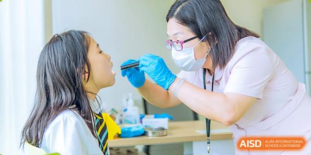 A medical professional or nurse at Hiba Academy Nantong examining a student's throat using a medical tool as part of a health check-up.