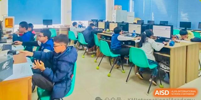 Students working on desktop computers in a brightly lit computer lab with teal chairs at Kunming International Academy.